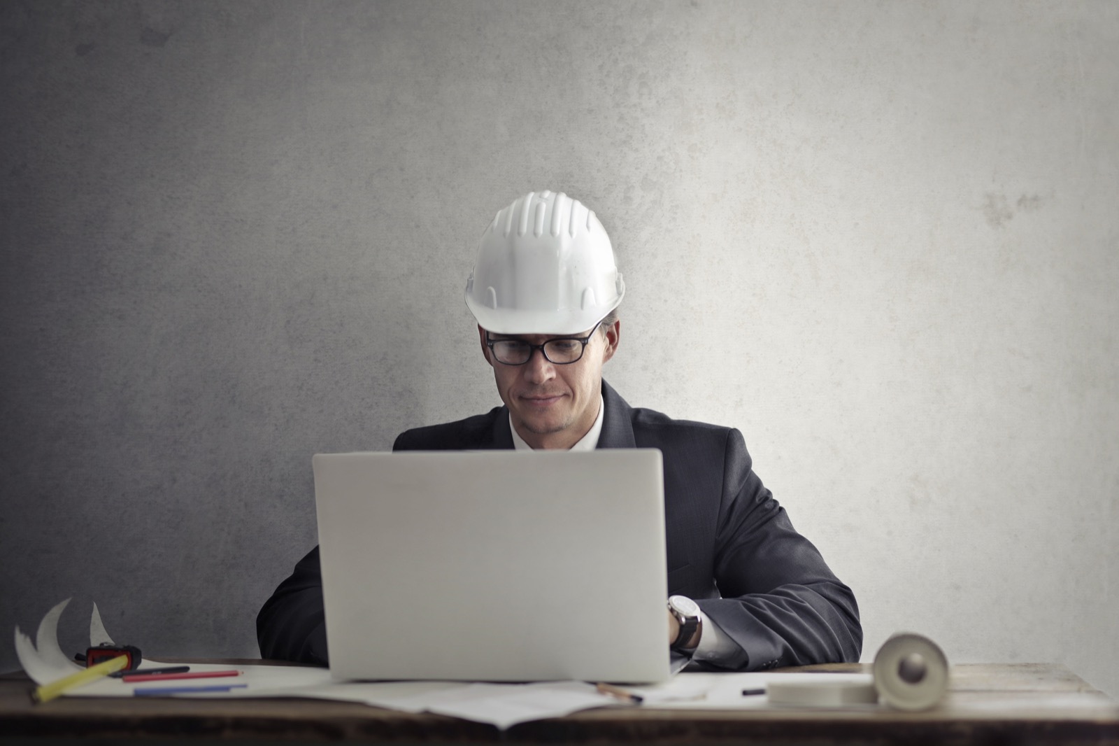 Contractor wearing a hard hat reviewing work on a laptop